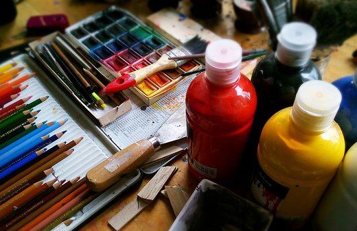 Art materials arranged on table - pencils crayons, paint palette, brushes and paint bottles.